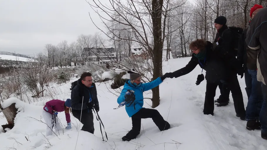 Menschen helfen sich im Schnee auf einem Waldweg.